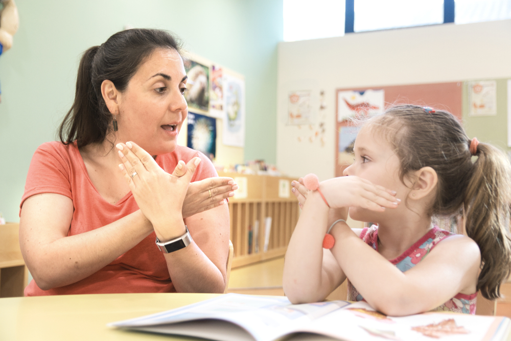 teacher teaching American sign language to student in school classroom